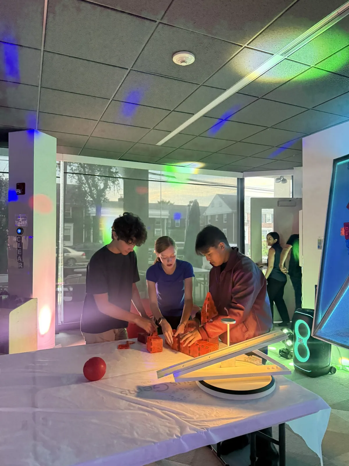 Teens building a marble run challenge under green and purple lights