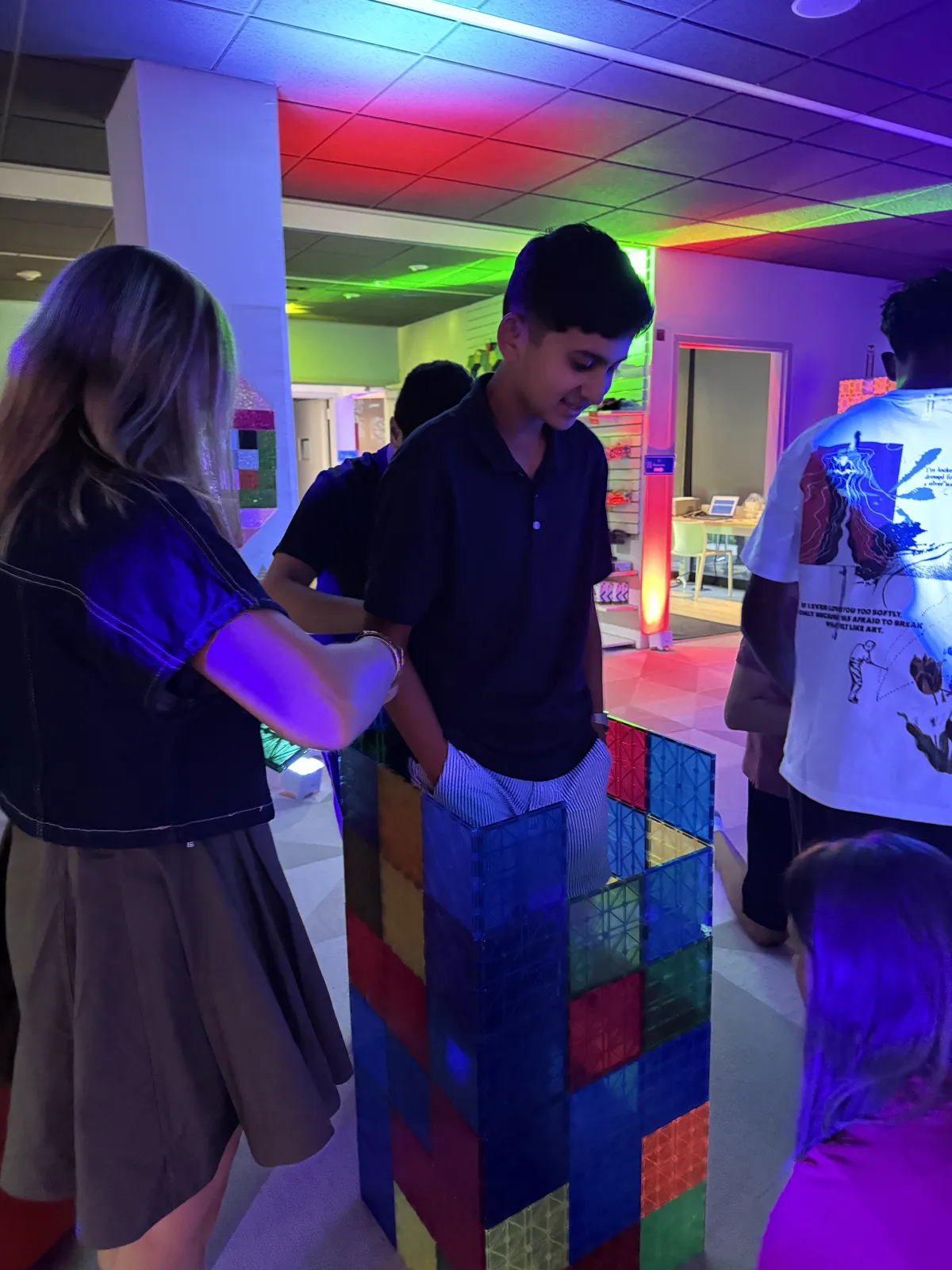 Teens stacking magnetic tile walls under neon lights
