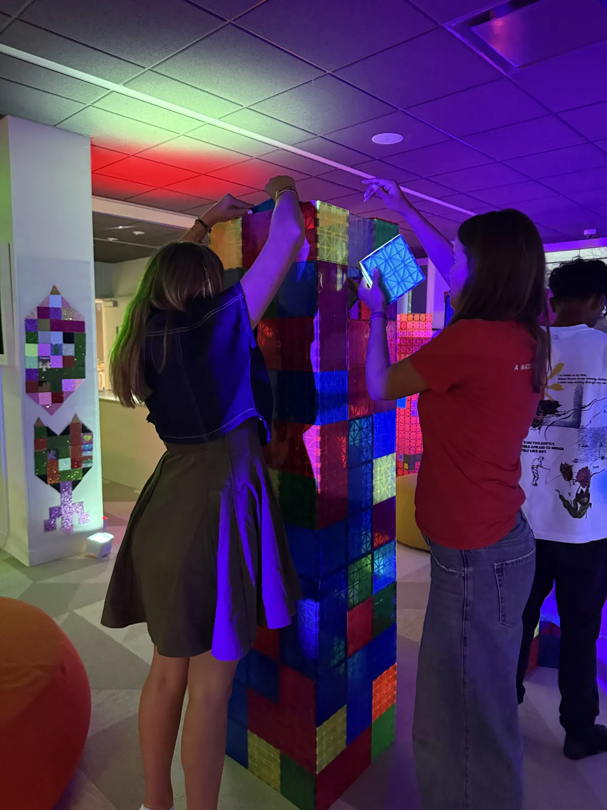 Two teens reaching up to finish a magnetic tile tower