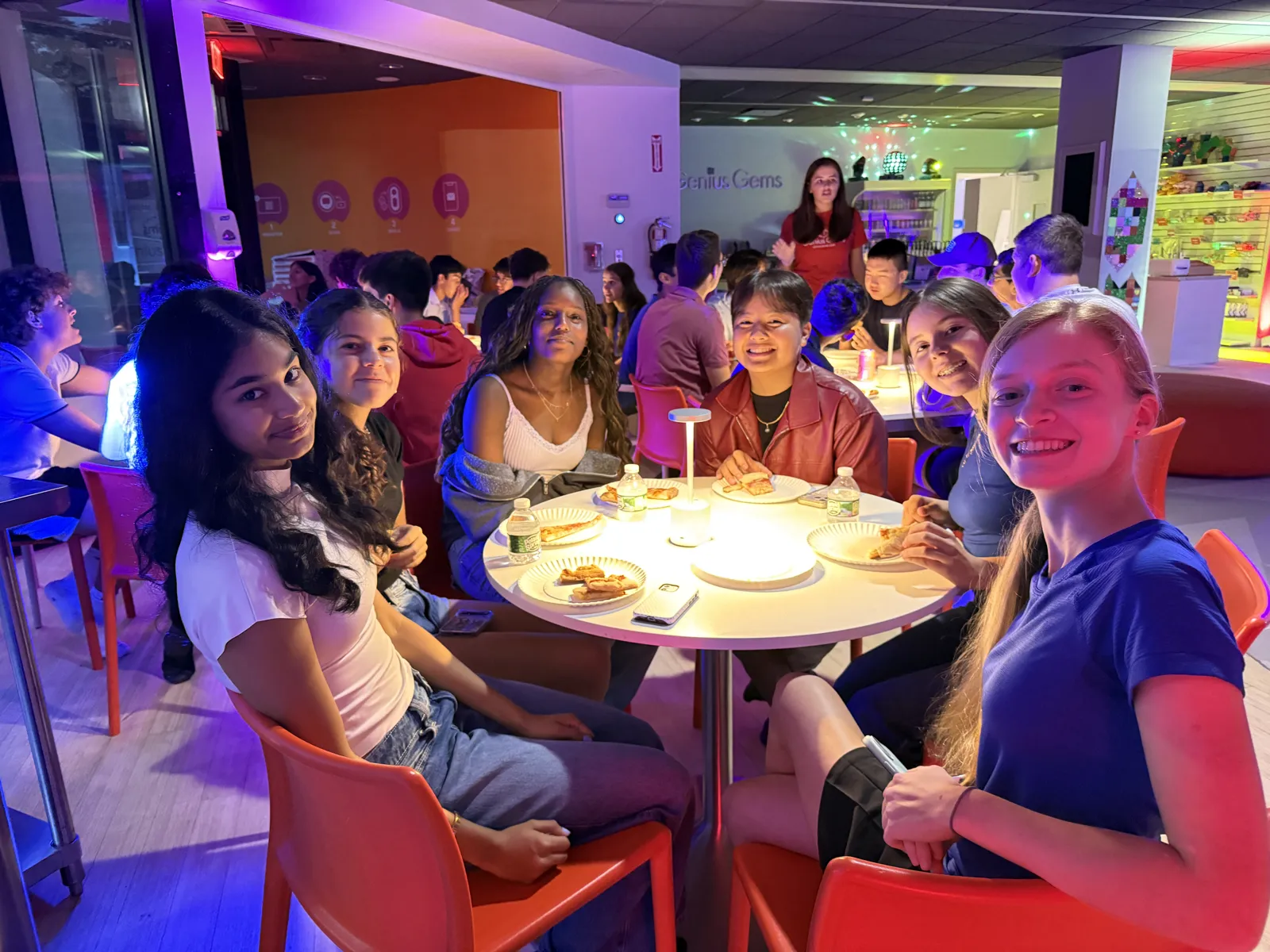 Teens smiling around a candlelit table under purple light